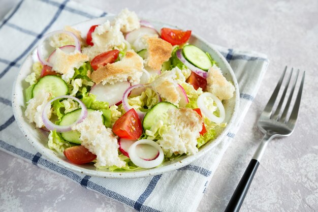 Fattoush de salade bouchent avec du pain pita grillé et des légumes dans la plaque blanche sur la serviette avec une fourchette.