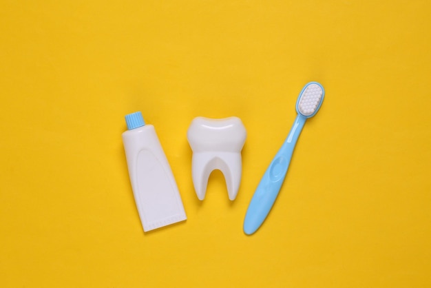 Fausse dent, brosse à dents et dentifrice sur fond jaune. Vue de dessus