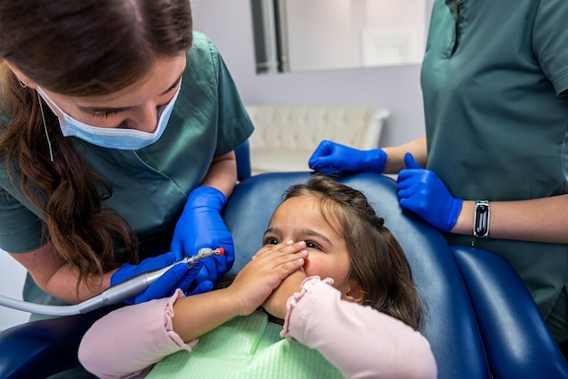 sur le fauteuil dentaire se trouve une petite fille qui est sur le point d'ouvrir la bouche au dentiste. Le concept de traitement dentaire chez les enfants