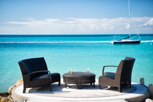 Fauteuils et table sur la plage tropicale à St Johns, Antigua. Meubles en rotin et yacht dans l'eau turquoise de la mer ou de l'océan. Vacances d'été dans les Caraïbes. Salon, luxe, concept de style de vie