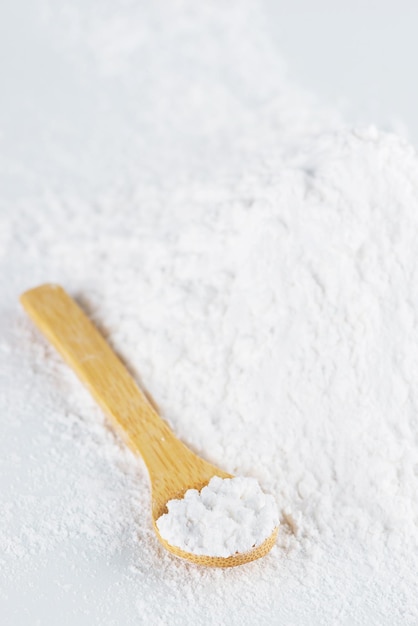 Fécule de tapioca blanche dans une cuillère en bois et éparpillée sur une table lumineuse