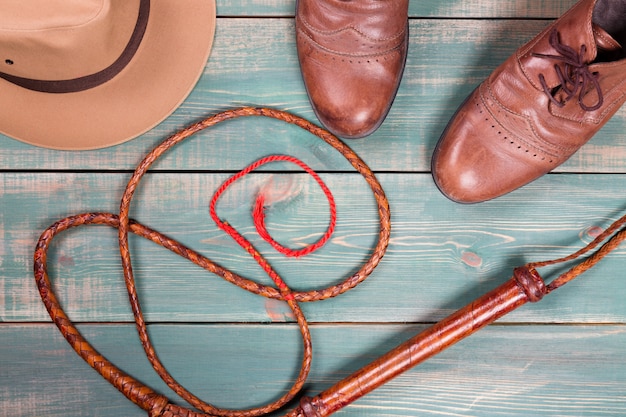 Fedora vintage, fouet et vieilles chaussures marron sur une table en bois verte