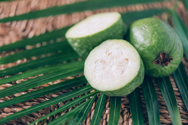 Feijoa de fruits tropicaux sur des feuilles de palmier sur fond de rotin Espace de copie Acca sellowiana Bannière de conception créative Heure d'été Voyage tropical fruits exotiques Concept végétalien et végétarien