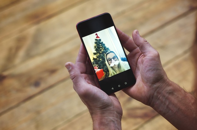 Félicitations de Noël en ligne Mans mains tenant un smartphone et discutant avec la famille