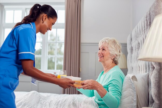 Photo female care worker en uniforme apportant une femme âgée à la maison le petit-déjeuner au lit sur le plateau