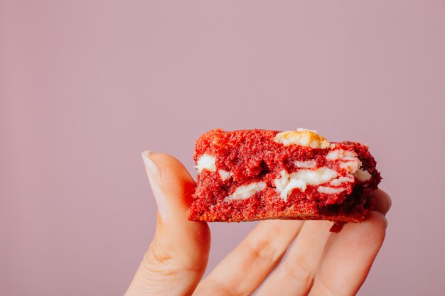 Female hand holding red velved cookie avec fond rose