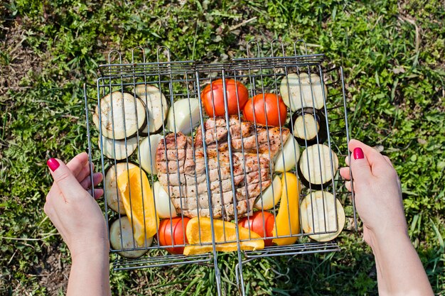 Femelle mains tenant des légumes appétissants et un steak de porc sur une grille