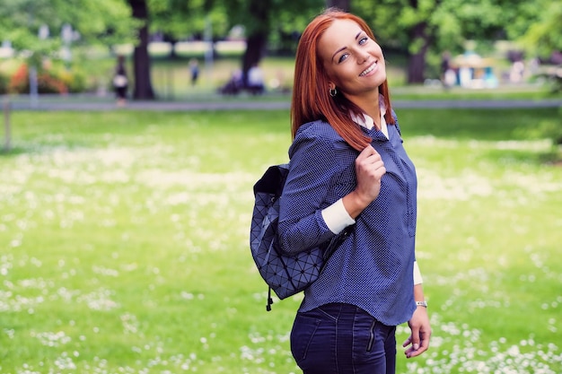 Femelle rousse positive avec sac à dos posant dans un parc d'été.