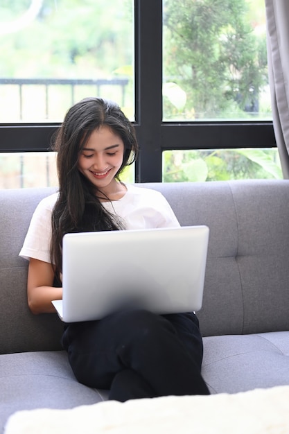 La femelle utilise un ordinateur portable et est assise sur un canapé