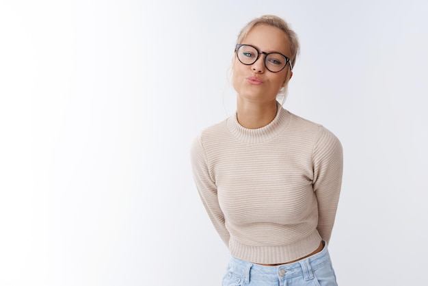 femme de 25 ans dans des lunettes et un pull court pliant la lèvre se penchant en avant envoyant un baiser flirter se sentir optimiste et sensuel sur blanc