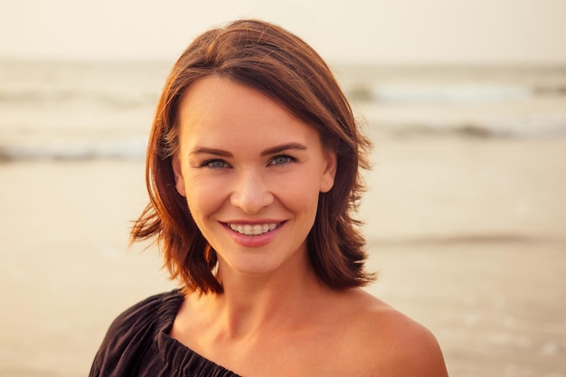 Femme, 30-35 ans, sourire à pleines dents souriant avec bretelles sur fond de plage mer océan.