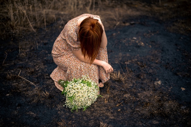 Femme de 40 ans avec un bouquet de fleurs sauvages sur la terre brûlée, concept d'épuisement psychologique