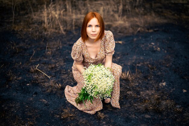 Femme de 40 ans avec un bouquet de fleurs sauvages sur la terre brûlée, concept d'épuisement psychologique