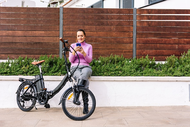 Femme de 40 ans, parlant au téléphone à côté de son vélo électrique