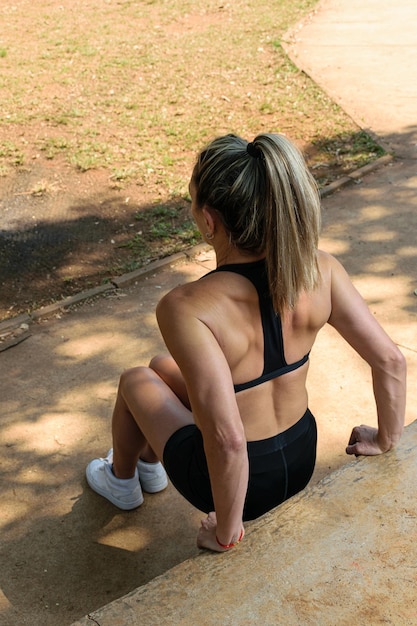 Femme de 42 ans faisant des exercices de triceps à l'aide d'un banc en béton, vue arrière (photo verticale).