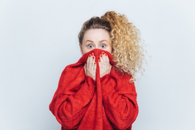 Une femme abasourdie et effrayée voit sa phobie, couvre le visage avec le col du pull rouge