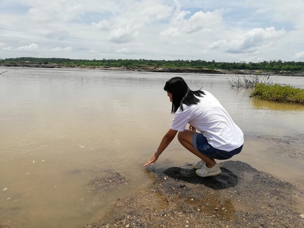 Photo une femme accroupi par la rivière contre le ciel