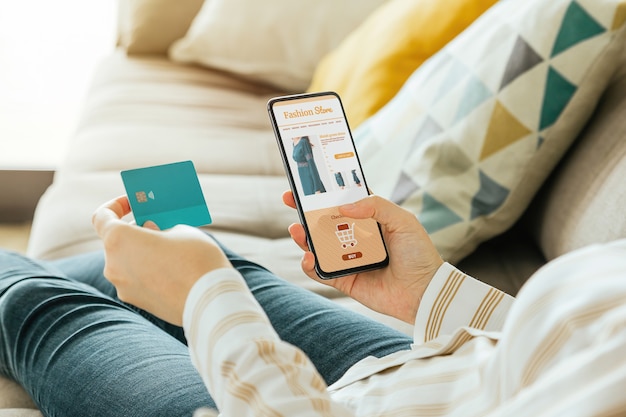 Femme achetant une robe en ligne avec le téléphone et une carte de crédit à domicile.