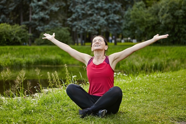 Femme active fait du yoga dans un parc public près de l'étang.