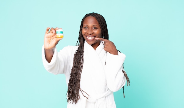 Femme adulte afro-américaine noire portant un peignoir et tenant des produits cosmétiques