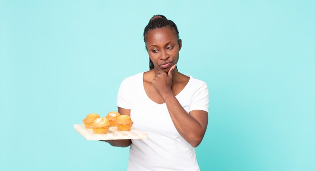 Femme adulte afro-américaine noire tenant un plateau à muffins