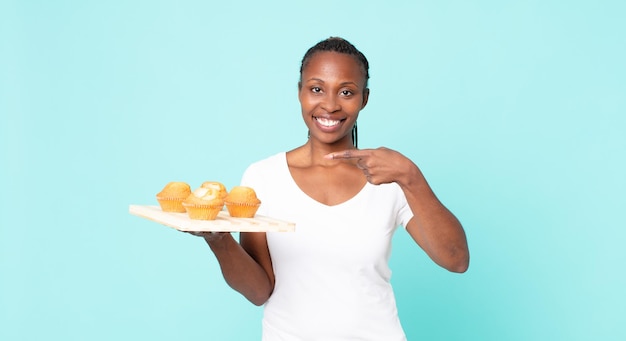 Femme adulte afro-américaine noire tenant un plateau à muffins