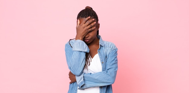 Femme adulte afro noire ayant l'air stressée, honteuse ou contrariée, avec un mal de tête, couvrant le visage avec la main