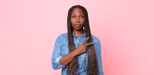 Femme adulte afro noire se sentant heureuse, positive et réussie, avec la main en forme de v sur la poitrine, montrant la victoire ou la paix