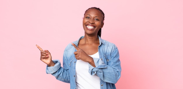 Femme adulte afro noire souriant joyeusement et pointant vers le côté et vers le haut avec les deux mains montrant l'objet dans l'espace de copie