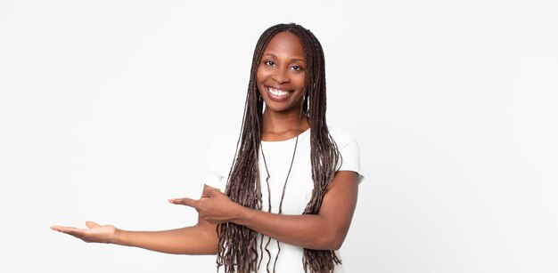 Femme adulte afro noire souriante, se sentant heureuse, insouciante et satisfaite, pointant vers le concept ou l'idée sur l'espace de copie sur le côté