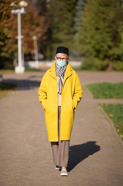 Femme adulte âgée dans le parc à l'automne dans un masque médical