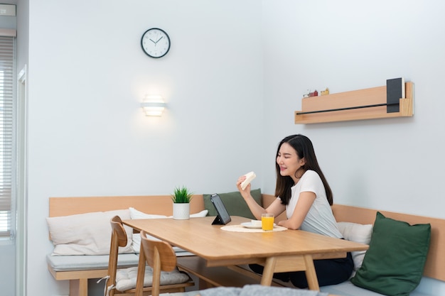 femme adulte appréciant de manger des sandwichs et du jus d'orange en regardant les médias en ligne