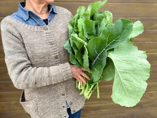 Femme adulte aux cheveux blancs courts tenant un bouquet de feuilles vertes Bouquet de légumes au chou