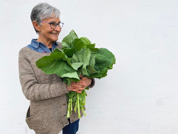 Femme adulte aux cheveux blancs courts tenant un bouquet de feuilles vertes Bouquet de légumes au chou