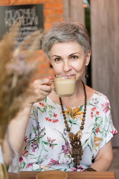 Une femme adulte aux cheveux gris. S'assoit dans un café et boit du café.