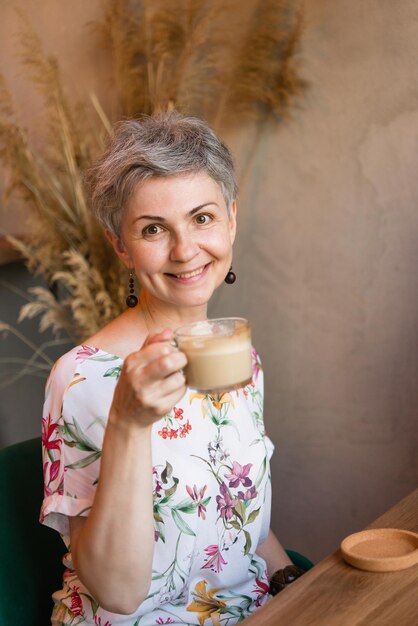 Une femme adulte aux cheveux gris. S'assoit dans un café et boit du café.