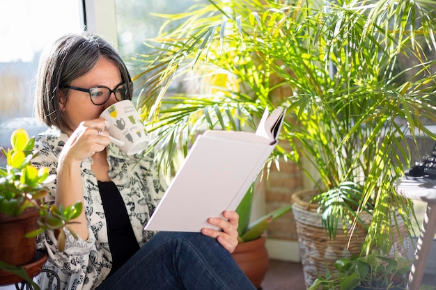 Femme adulte buvant du café et lisant un livre dans le jardin Moment de plaisir et de tranquillité à la maison