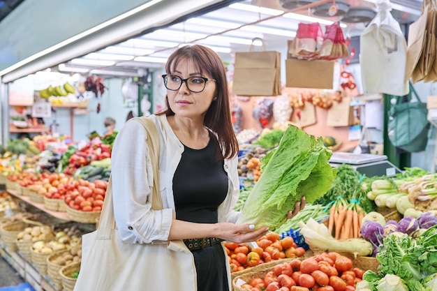 Une femme adulte choisit d'acheter des buissons de laitue au marché des agriculteurs