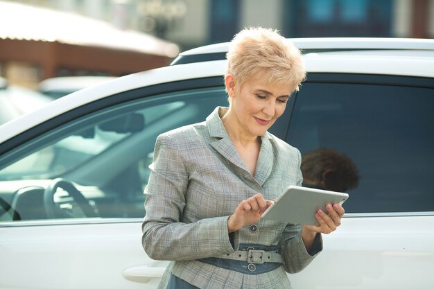 femme adulte élégante en costume avec tablette près de voiture