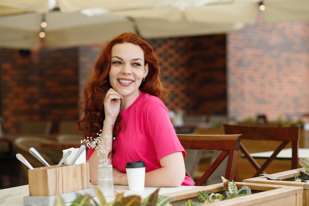 Une femme adulte est assise dans un café d'été avec une tasse de café et souriant