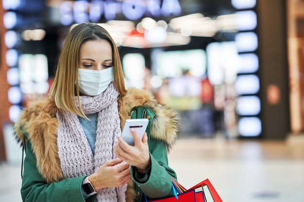 femme adulte faisant ses courses dans un centre commercial à l'aide d'un smartphone portant un masque, concept de coronavirus
