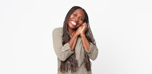 femme adulte noire afro se sentant amoureuse et ayant l'air mignonne, adorable et heureuse, souriante de manière romantique avec les mains à côté du visage