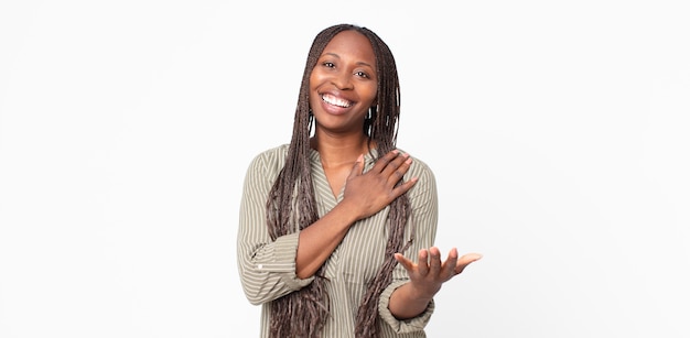 Photo femme adulte noire afro se sentant heureuse et amoureuse, souriante d'une main à côté du cœur et de l'autre tendue vers l'avant