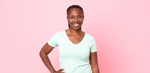 Femme adulte noire afro souriante joyeusement avec une main sur la hanche et une attitude confiante, positive, fière et amicale
