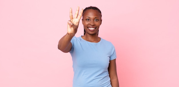 Femme adulte noire afro souriante et semblant amicale, montrant le numéro trois ou troisième avec la main vers l'avant, compte à rebours