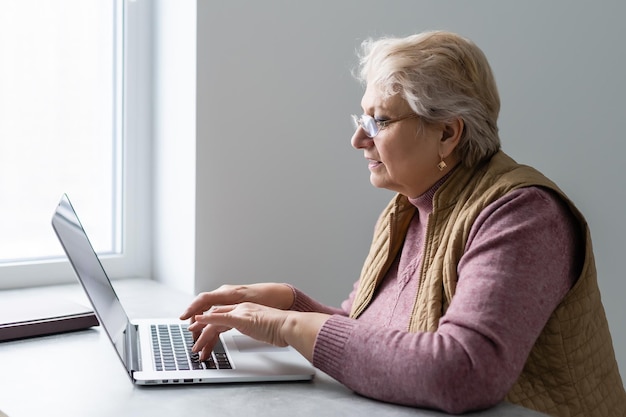 Femme adulte plus âgée sérieuse regardant un webinaire de formation sur un ordinateur portable travaillant à domicile ou au bureau. Femme d'affaires d'âge moyen des années 60 prenant des notes tout en utilisant la technologie informatique.