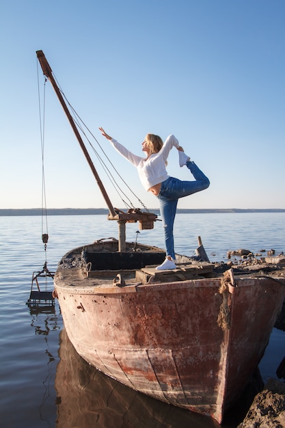 Femme adulte pratique le yoga sur un vieux bateau sur la plage