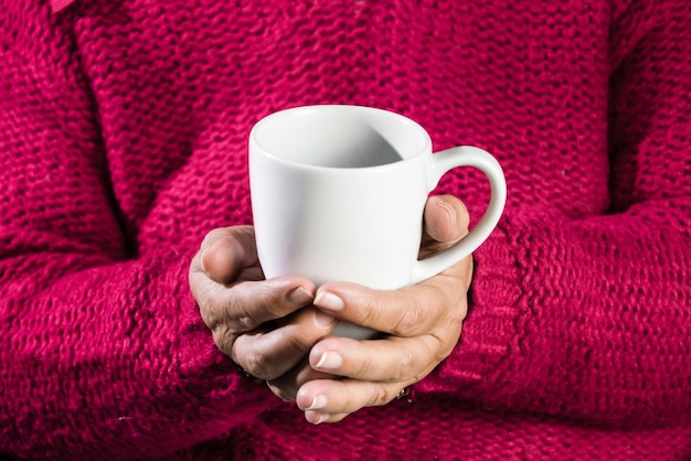 Femme adulte avec pull rouge tenant une tasse de café au lait.