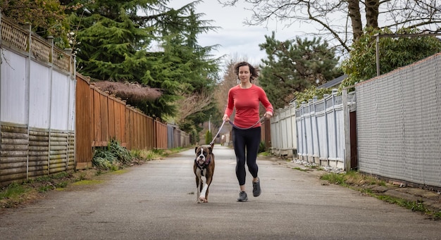 Femme adulte de race blanche athlétique courant à l'extérieur avec un chien Boxer