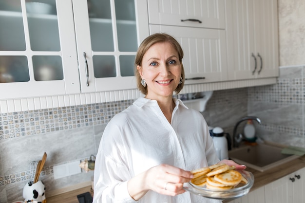 Une femme adulte se tient dans la cuisine et tient des crêpes dans ses mains